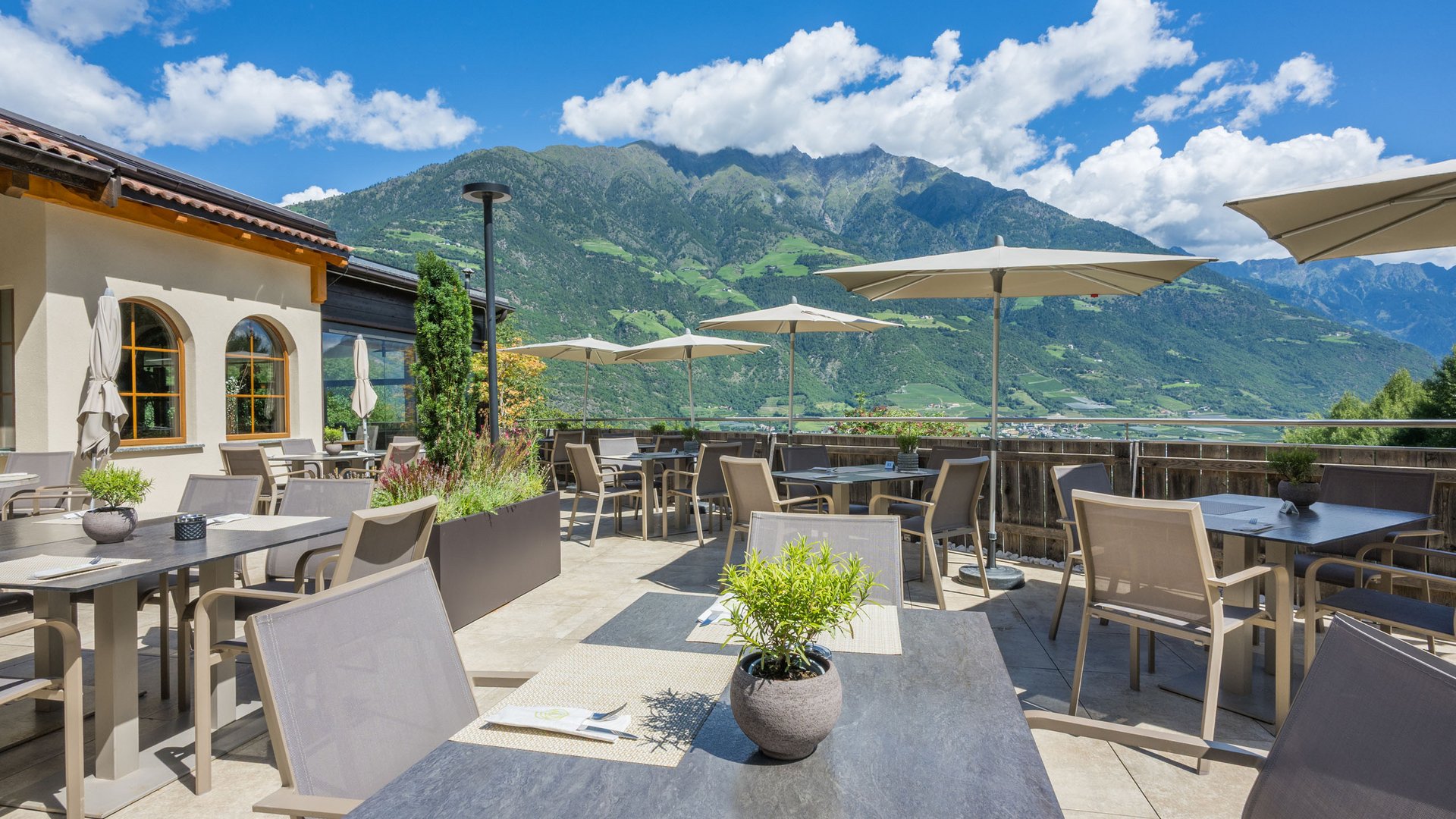 Ramilia: euer Lokal für Geburtstagsfeiern und mehr Terrasse mit Tischen und Sonnenschirmen vor grünen Bergen und blauem Himmel