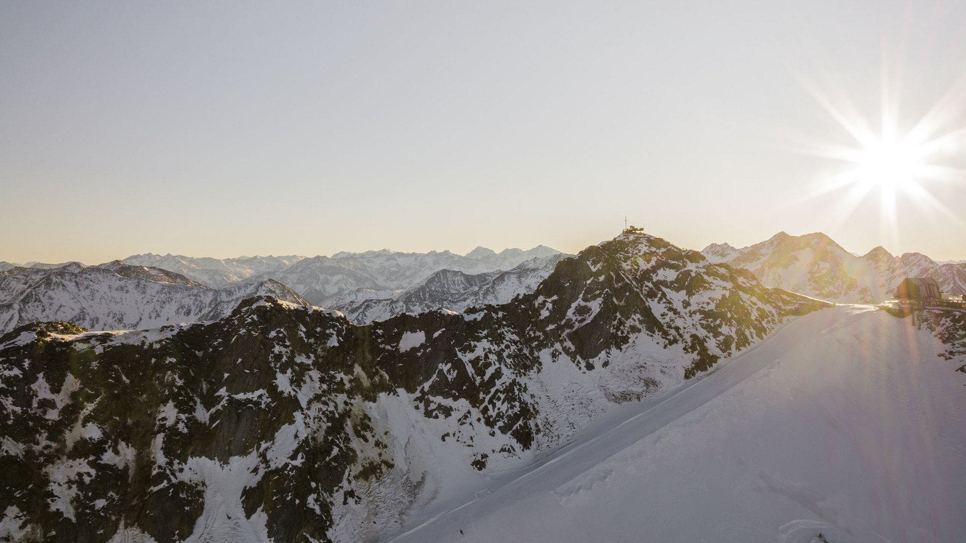 Sonniger Himmel über schneebedeckten Alpenbergen mit Gipfelkreuz
