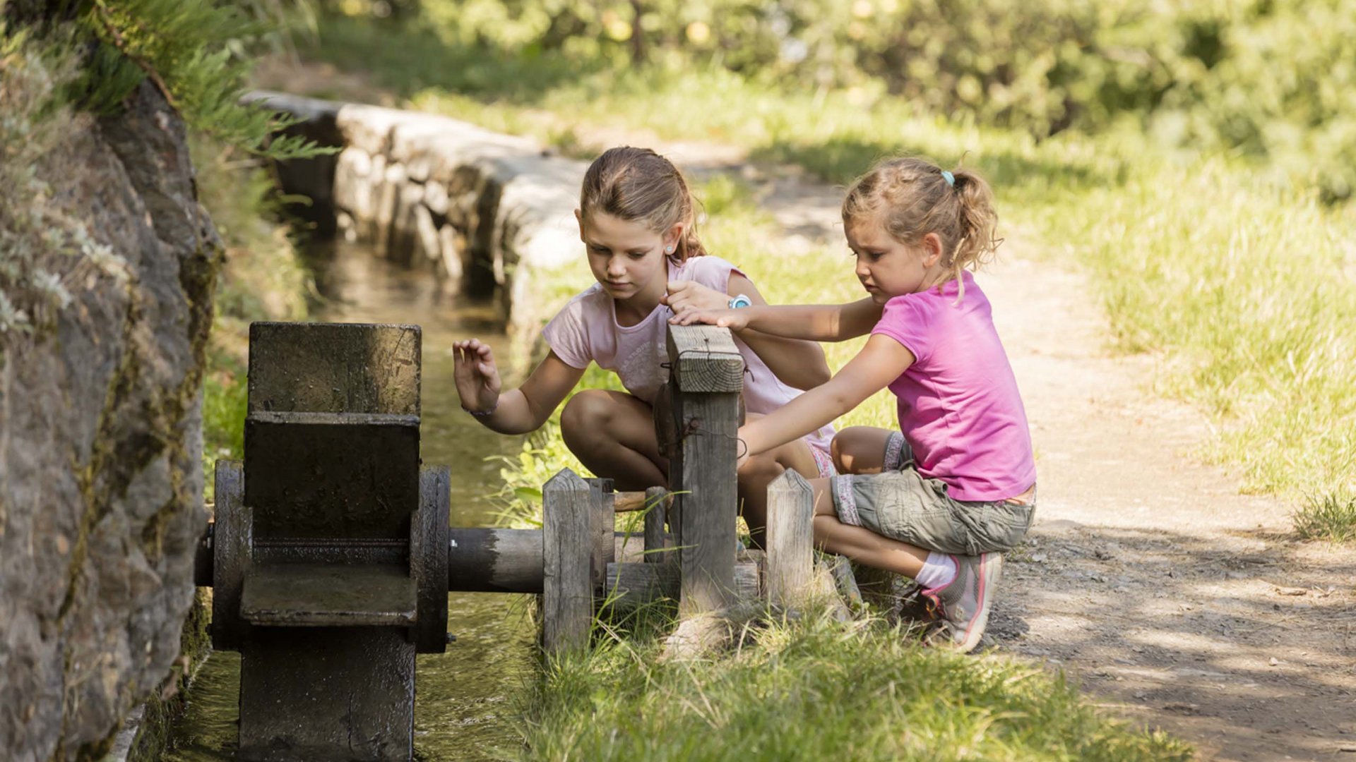 Nature holidays in Naturns Two girls playing with water at a water wheel outdoors